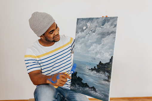 Black man artist sitting on the chair and looking at his painting