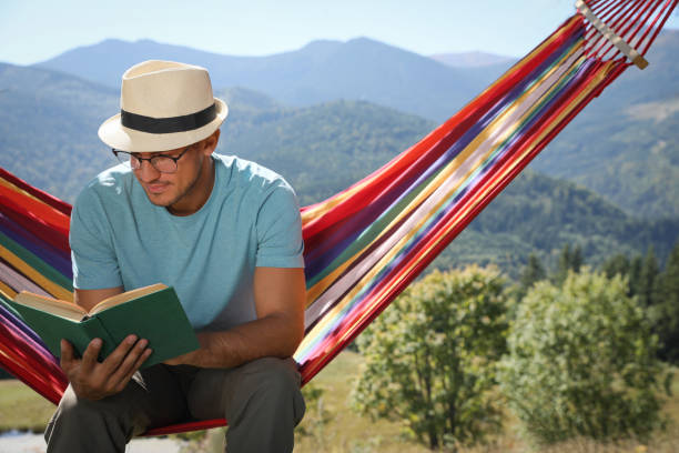 istock Handsome man reading book in hammock outdoors on sunny day 1402845410