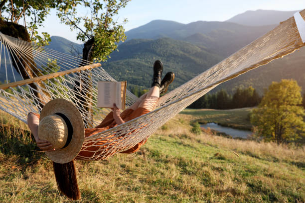 Young woman reading book in hammock outdoors at sunset