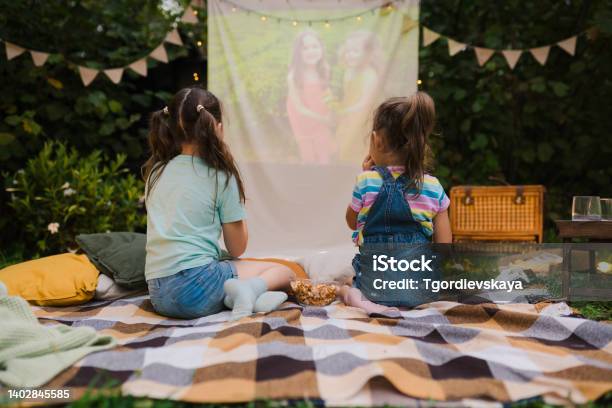 Backyard Family Outdoor Movie Night With Kids Sisters Spending Time Together And Watching Cimema At Backyard Diy Screen With Film Summer Outdoor Weekend Activities With Children Open Air Cinema Stock Photo - Download Image Now