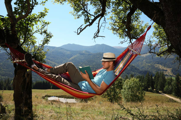 istock Handsome man reading book in hammock outdoors on sunny day 1402845649