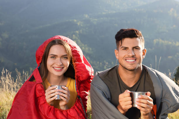 istock Happy couple with drinks in sleeping bags surrounded by beautiful nature 1402846791