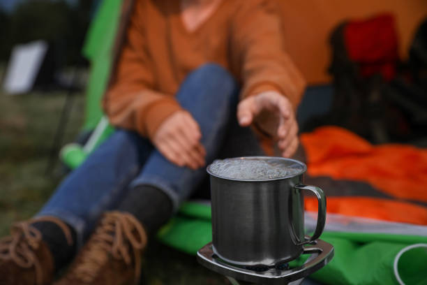 istock Woman taking cup off stove while sitting in camping tent outdoors, closeup 1402846868