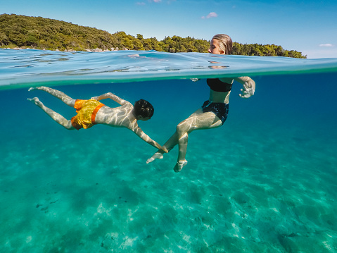 Boy playing with his sister in the emerald green sea, pulling her leg under water, taken with wearable waterproof camera