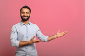 Handsome Indian guy points palms at empty copy space isolated on pink