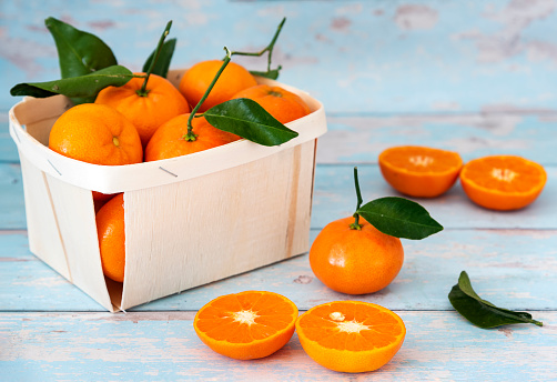 Satsuma Mandarin cut up in the foreground. A box of Satsuma Mandarin in an environmentally friendly box in the background. The photograph is taken against a blue background to give a Mediterranean feel.