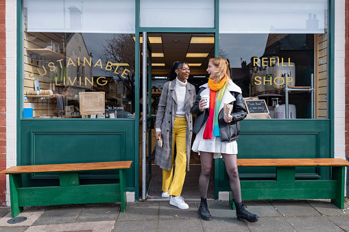 Two friends leaving a store with smiles that promotes sustainable living in the North East of England. The store has refill stations to reduce plastic and food waste. The store sells homemade organic bars of soap as well as vegan based foods.