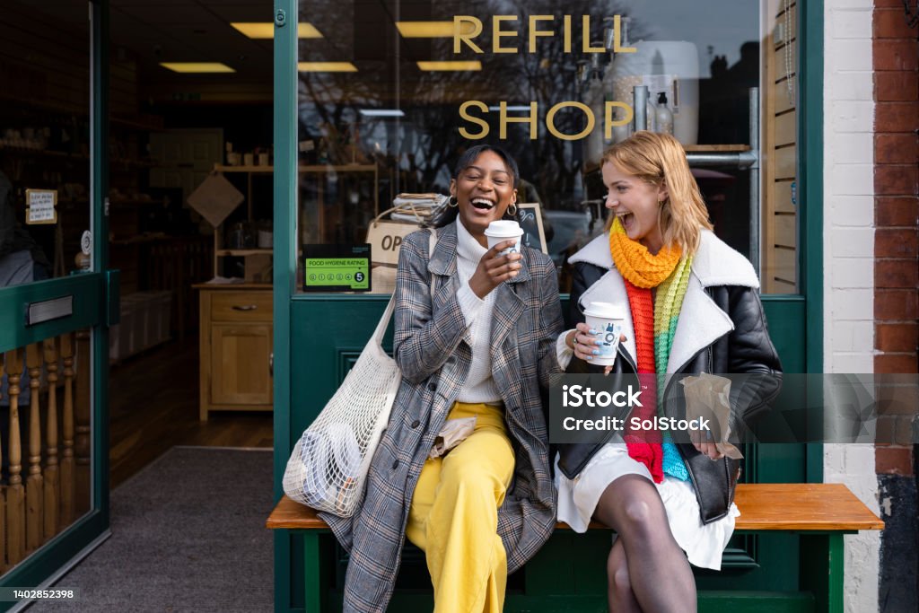 Coffee and Laughs Two friends sitting outside a store that promotes sustainable living in the North East of England. The store has refill stations to reduce plastic and food waste. The store sells homemade organic bars of soap as well as vegan based foods. Friendship Stock Photo