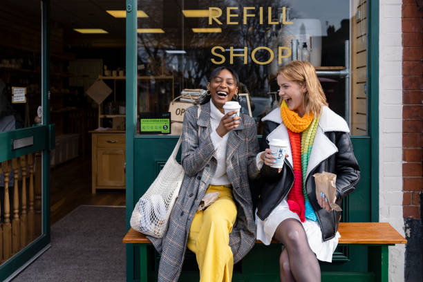 Coffee and Laughs Two friends sitting outside a store that promotes sustainable living in the North East of England. The store has refill stations to reduce plastic and food waste. The store sells homemade organic bars of soap as well as vegan based foods. friendship stock pictures, royalty-free photos & images