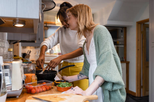 Adding More Flavour Two friends maintaining their sustainable living by preparing a vegan meal in the kitchen in the North East of England. One young woman is cooking chopped onions in the pan and adding hot curry powder while her friend stands with her. only young women stock pictures, royalty-free photos & images