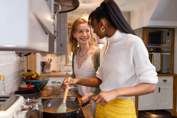 Making a Tasty Curry Two friends maintaining their sustainable living by preparing a vegan meal in the kitchen in the North East of England. One young woman is cooking a dhal curry in the pan while her friend stands with her with a big smile. only young women stock pictures, royalty-free photos & images