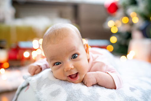 Baby girl lying on blanket against Christmas lights at home