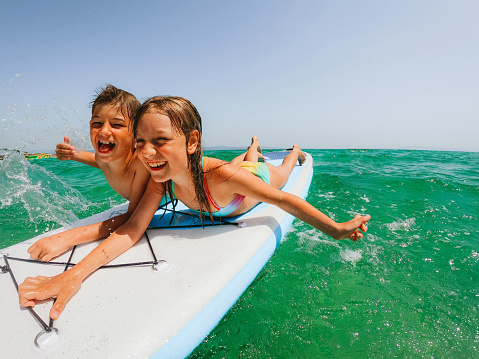 Photo of brother and sister having fun while enjoying together on a paddleboard in the sea.