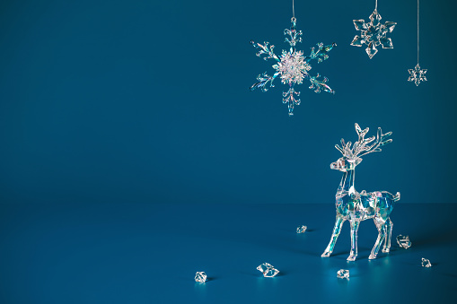 Winter scene with Christmas decorations made of crystal glass. Xmas deer and snowflakes on dark blue background with copy space, front view.