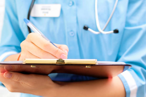 cropped view of female doctor in uniform with stethoscope holding clipboard and writing records and diagnosis in medical card or patient history in hospital, medical consultation. close-up - doctor electronic organizer healthcare and medicine patient imagens e fotografias de stock