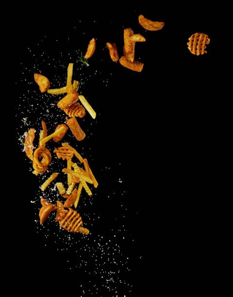Assorted fries falling in studio Various types of tasty unhealthy high calorie fries with white salt falling against black background in modern light studio curly fries stock pictures, royalty-free photos & images