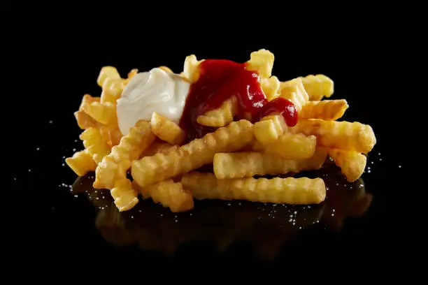 High angle of appetizing crinkle cut French fried with mayonnaise and ketchup on black glossy table
