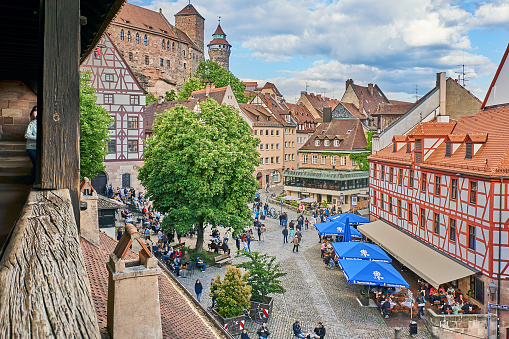 Nuremberg, Germany - May 28, 2022: Crowd at the Tiergärtnertor in Nuremberg. On the left part of the old city wall and on the right the Albrecht Dürer house. In the background the towers of the Kaiserburg.