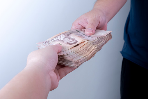 Imagen de la mano de un hombre dando una gran cantidad de dinero a la mano de una mujer (billetes tailandeses) photo