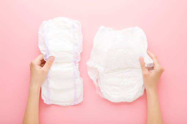 Young adult woman hands holding white big size sanitary towel and diaper pant on pastel pink background. Closeup. Hygiene product for urinary incontinence or after childbirth. Top down view. Young adult woman hands holding white big size sanitary towel and diaper pant on pastel pink background. Closeup. Hygiene product for urinary incontinence or after childbirth. Top down view. adult diaper stock pictures, royalty-free photos & images