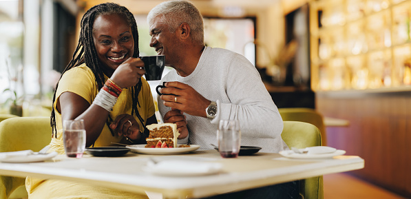 Happy senior couple smiling cheerfully while eating together in a coffee shop. Carefree senior couple having a good time in a restaurant. Mature couple enjoying their retirement together.