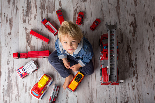 Child, toddler blond boy, playing with fire trucks on the floor at home