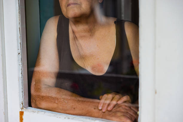 Lonely senior Caucasian woman looking through window, feeling pensive and nostalgic