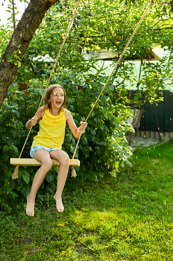 Happy barefoot laughing child girl swinging on a swing in sunset summer day on the backyard at home, summertime outdoor, vacation.