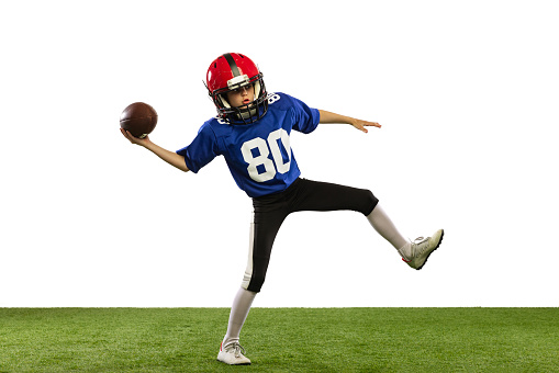 Workout. Sportive little boy in sports uniform and equipment playing american football isolated on white background with green grass flooring. Concept of sport, ad, movement, achievements.