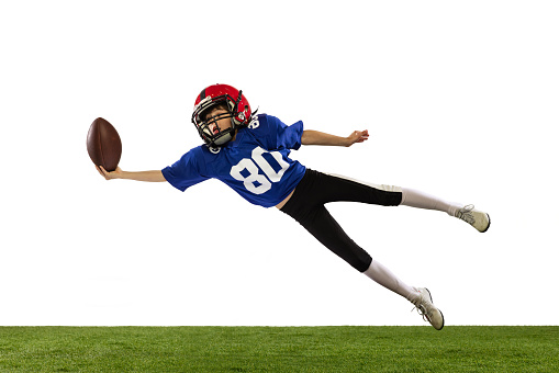 Dynamic portrait of little boy, beginner player of american football training isolated on white background with green grass flooring. Concept of sport, movement, achievements. Copy space for ad