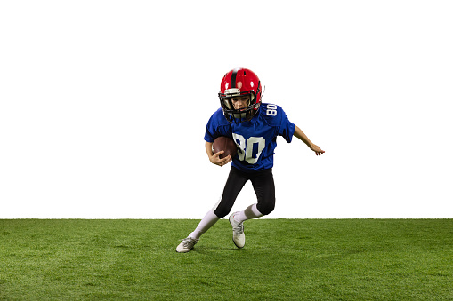 In motion. Athletic kid, beginner american football player in sports uniform and helmet training isolated on white background. Concept of sport, challenges, action, achievements.