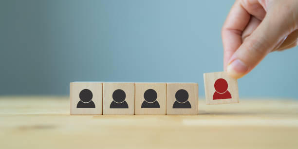 istock Human resource management, recruitment and target customer business concept. Man's hand puts wooden cube red person which standing on crowd with black person symbol. Blue background and copy space. 1402887685