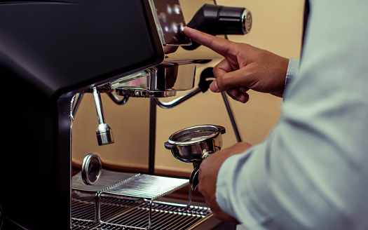 Selective focus and close up on barista's hands preparing coffee for customers and using equipment, pressing machine for brewing in indoor cafe shop. Business and Beverage Concept