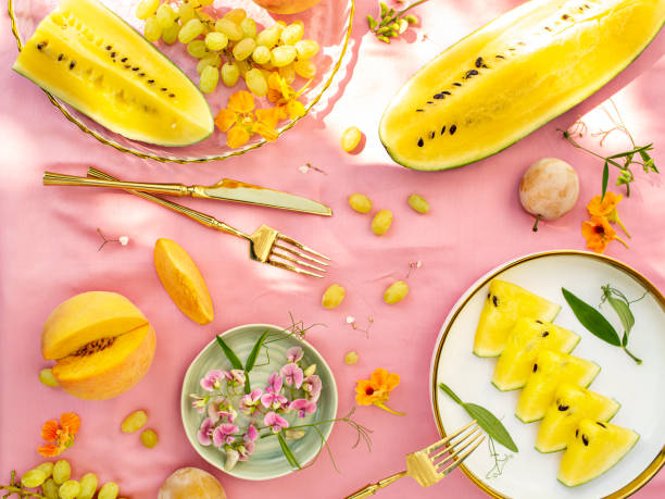 istock Sunny and bright open air breakfast with yellow watermelon, grape, plums and summer wild flowers decoration. Romantic picnic for couple. Floral botanical background, pattern. 1402891253
