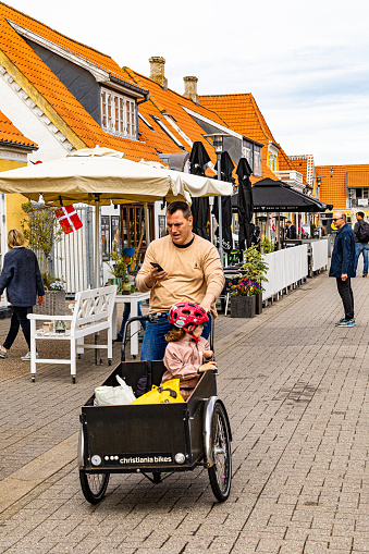 Skagen, Denmark June 7, 2022 A man rides a cargo bike with his child on the main street.