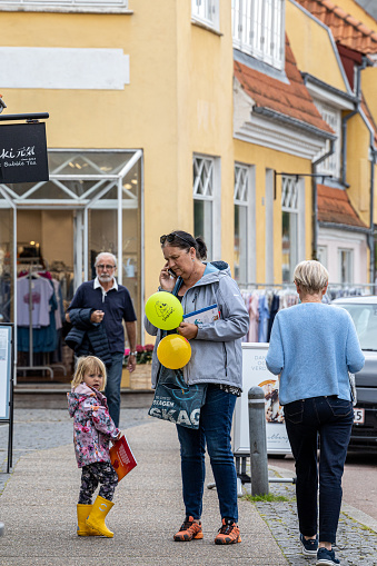 Skagen, Denmark June 7, 2022 A woman with her daughter holding yellow balloons speaks on the phone.