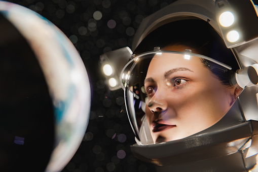 3D rendering of concentrated young female astronaut in modern gray spacesuit looking at planet during space expedition