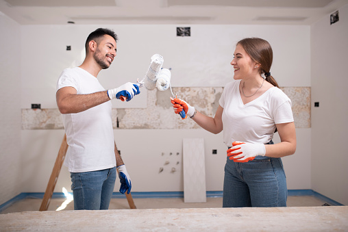 Renovation worker couple bump paint rollers amicably before painting their home