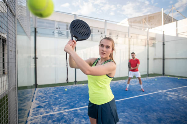 Woman playing paddle tennis in court. Man in background. stock photo