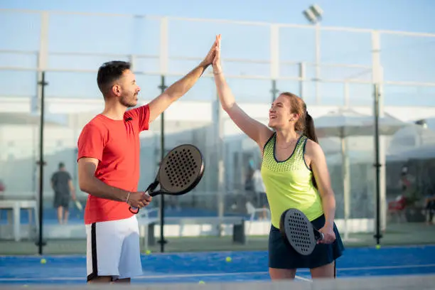 Couple playing paddle tennis in court, hi five fair play gesture