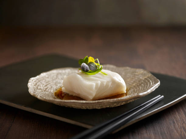 Steamed Cod Fish with Supreme Soya Sauce served in a dish isolated on wooden board side view dark background stock photo
