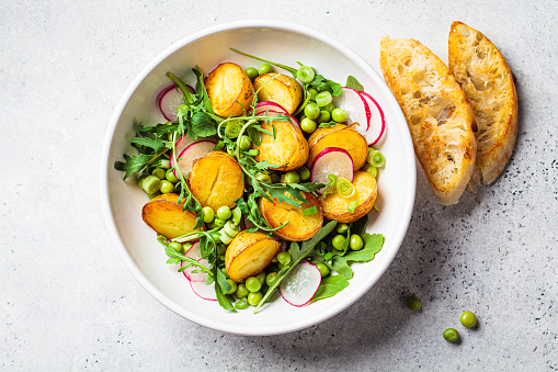 Summer potato and pea salad with arugula and radish in a white bowl, top view. Vegan recipe.
