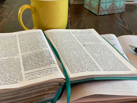 Bible laying open with teal colored book marks. Passage underlined in black ink. Yellow coffee mug, notebook and pen in the background