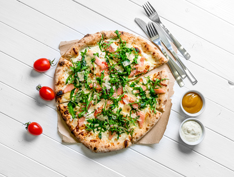 Top view of tasty Italian pizza with cutlery and sauces on white rusric wooden background