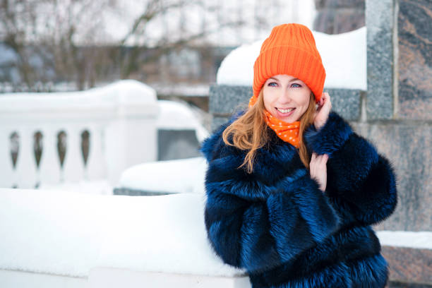 Portrait Attractive Girl Walking in Winter Park. Young Woman in Stylish Warm Outfit and Orange Beanie Hat Posing Outdoors.