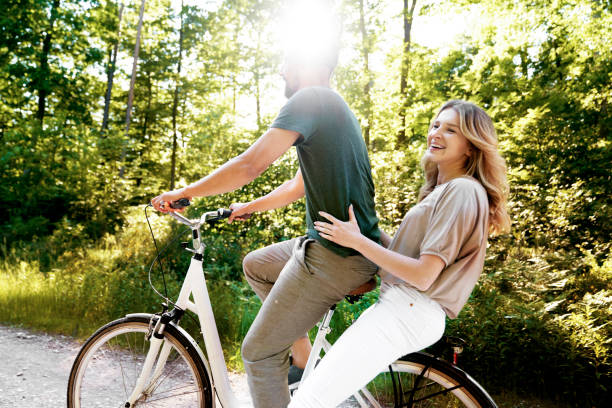 istock Side View Of Smiling Couple Sitting On Bicycle Against Trees 1402906262