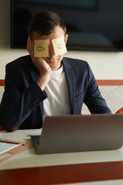 istock Bored worker fooling around with stickers on his eyes 1402914365