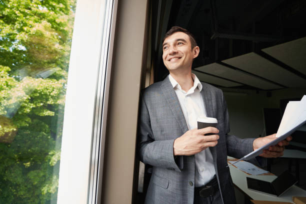 istock Satisfied male office worker with coffee looking into window 1402914395