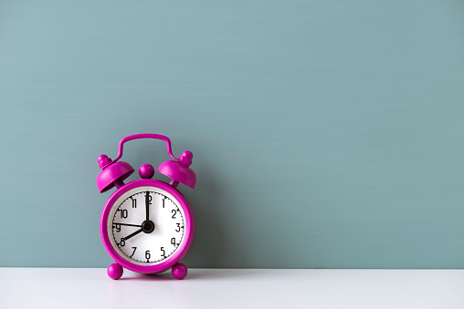 Pink alarm clock on white table in front of green
 colored wall. The clocks time is showing 8.