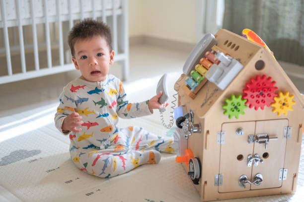 istock Baby boy playing with large activity box in the bedroom while sitting on a baby safe soft playmat on the floor at home. 10 months old infant playing at home 1402921794